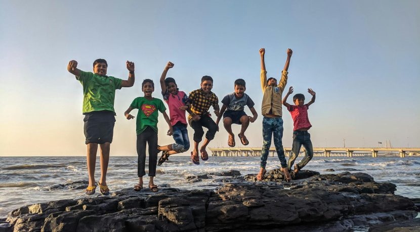 boy wearing green crew neck shirt jumping from black stone on seashore